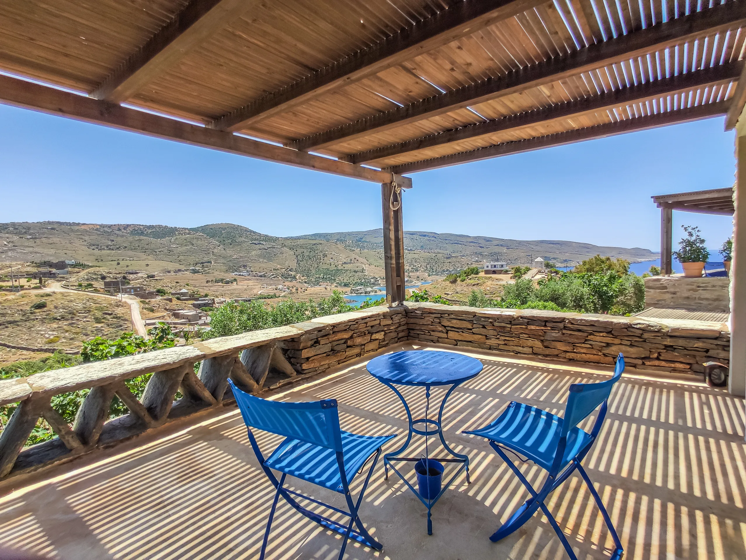 Pergola terrace with blue bistro chairs overlooking Koundouros bay and the Aegean, Zephyros Stone Villa, Kea